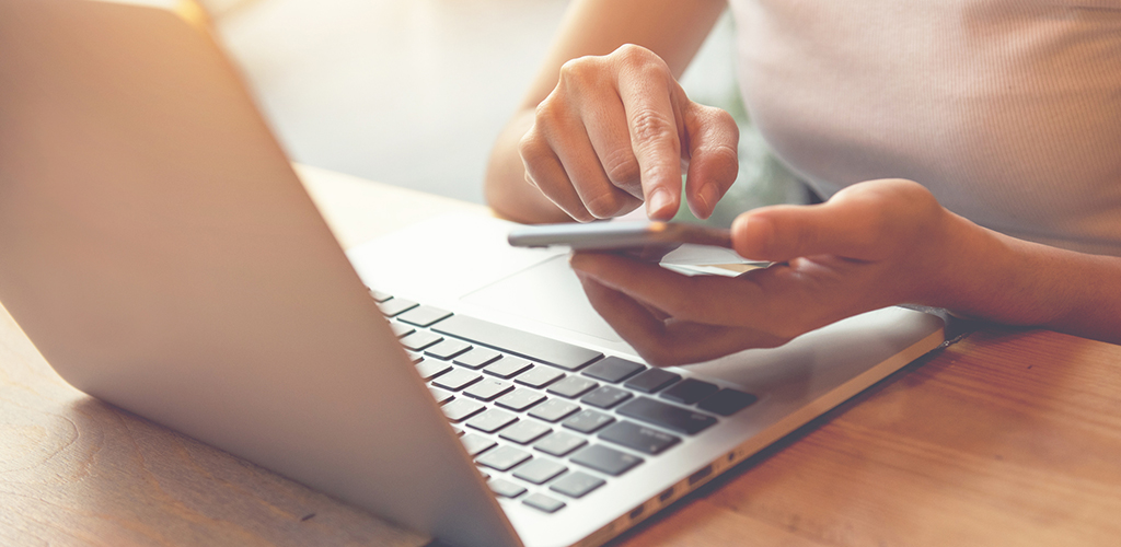 A person using a mobile phone while sat at a laptop.