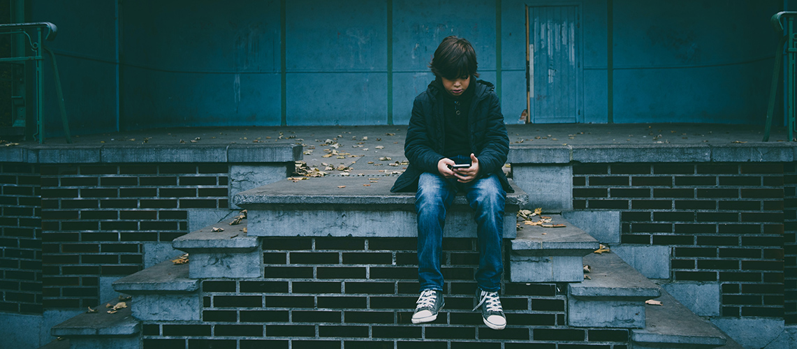 A boy sitting on concrete stairs looking at a mobile phone (photo by Gaelle Marcel on unsplash)