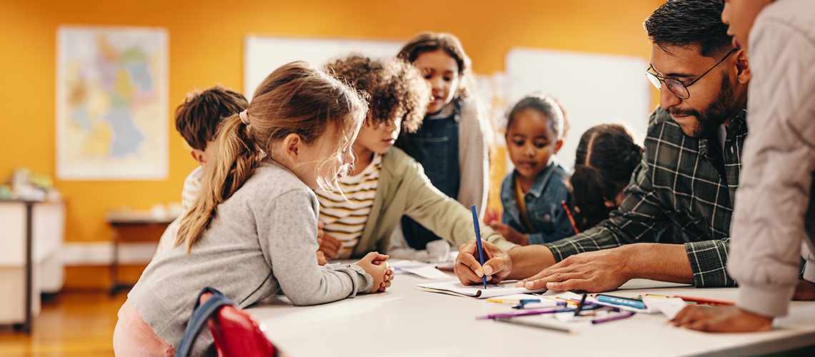 Children and an adult sitting around a table writing in notebooks