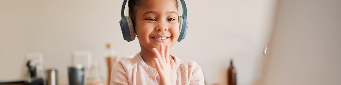 A young girl wearing headphones at a computer and smiling