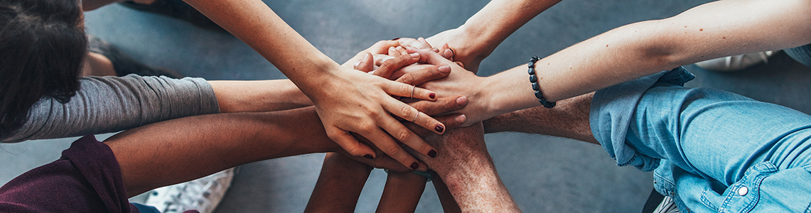 A huddle of people putting their hands together in a circle A huddle of people putting their hands together in a circle
